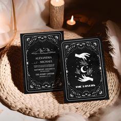 two black and white cards sitting on top of a table next to a candle with candles in the background