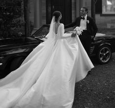 a bride and groom standing in front of a classic black car on their wedding day