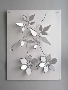 a metal wall sculpture with flowers on the front and back of it, hanging on a gray wall