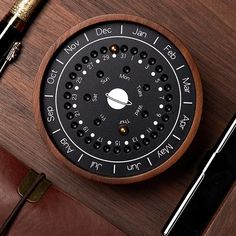 a wooden clock sitting on top of a desk next to a pen