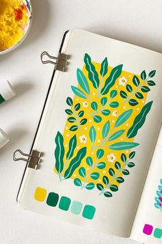 an open notebook with a pineapple drawn on it next to some markers and paintbrushes