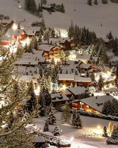 the town is lit up at night in the snow covered mountains and trees with lights on them