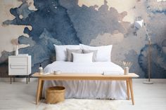 a bed with white sheets and pillows in front of a blue wall painted with watercolors