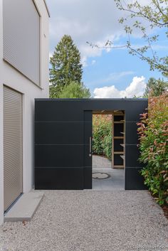 an open door leading into a courtyard with trees in the back ground and bushes on either side