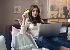 a woman sitting on a couch holding a credit card and looking at her laptop