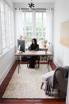 a woman sitting at a desk in front of a computer monitor on top of a wooden table