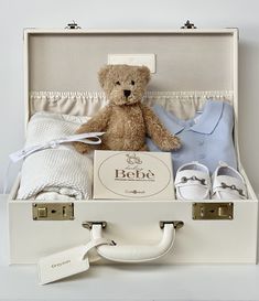 a teddy bear sitting on top of a suitcase filled with baby clothes and shoes,