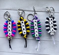 four different key chains with letters and beads attached to them on a white surface,