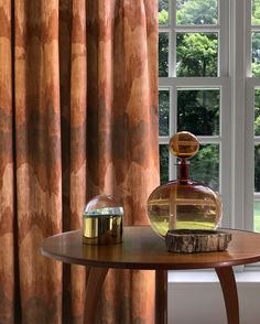 a table with a bottle on it next to a window and some curtains in the background