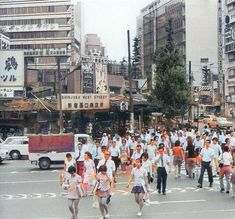 a group of people walking across a street next to tall buildings