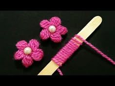 two crocheted flowers and a knitting needle on a black surface with pink yarn