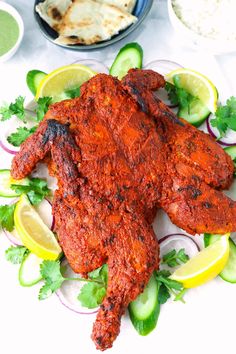 whole roasted tandoori chicken on a plate with cucumbers and lemon wedges