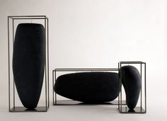 three black vases sitting next to each other on top of metal stands in front of a white wall