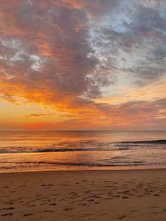 the sun is setting at the beach with footprints in the sand and on the water