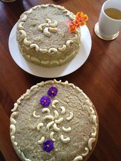 two cakes sitting on top of a wooden table next to cups and utensils