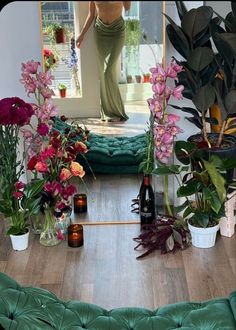 there is a woman standing in the mirror with flowers and bottles on the floor next to her