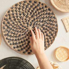 a person touching the side of a woven basket on top of a white table next to plates and baskets