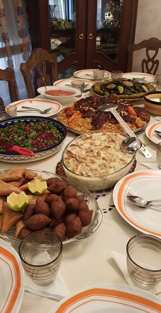 a table filled with lots of food on top of white tables cloth covered in orange and white plates