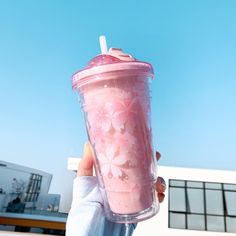 a person holding up a pink drink in front of a building with a blue sky