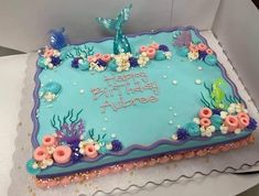 a birthday cake with blue frosting and pink flowers on the bottom is sitting in a box