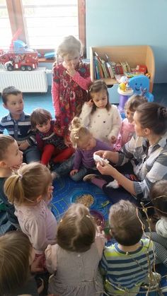 a group of children sitting on the floor in front of an older woman holding a cell phone