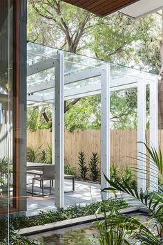 the inside of a house with glass walls and plants on the outside wall, surrounded by greenery