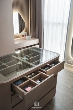 a glass table with drawers underneath it in front of a large mirror and curtained window