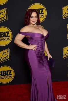 a woman in a purple dress standing on a red carpet with her hands on her hips