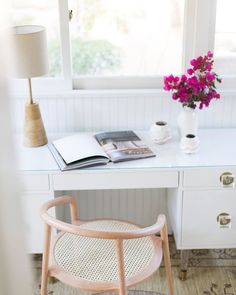 a white desk with a pink flower in a vase on it and a book next to it