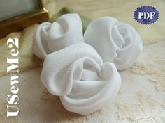 three white fabric flowers sitting on top of a lace covered table cloth next to a gold frame