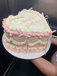 a heart shaped cake is being held by a woman's hand with pink ribbon