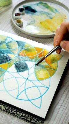 a person is drawing on paper with colored pencils and watercolor paints in the background