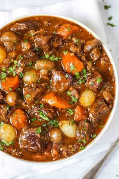 a white bowl filled with stew and carrots on top of a napkin next to a fork