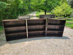 two wooden bookshelves sitting on top of a gravel road next to a forest