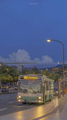 a green and white bus driving down a street next to a traffic light at night