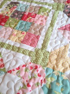 a close up of a patchwork quilt on a bed with white and pink sheets