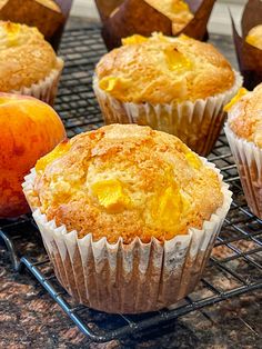 several muffins cooling on a wire rack with an apple and orange in the background