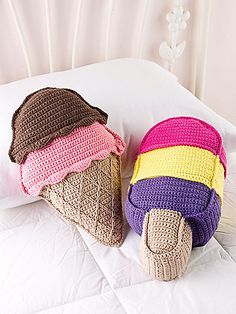 two crocheted ice cream cones are laying on a bed with white sheets and pillows