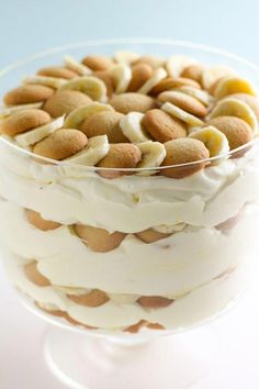 a layered cake with white frosting and almonds in a glass dish on a table