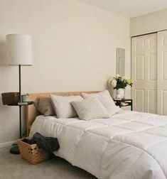 a bed with white sheets and pillows next to a lamp on a table in front of a closet