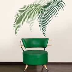 a green chair sitting on top of a wooden floor next to a palm leaf wall decal