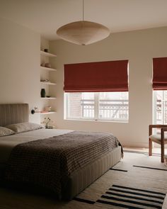 a bed sitting in a bedroom next to a window with red shades on it's windowsill