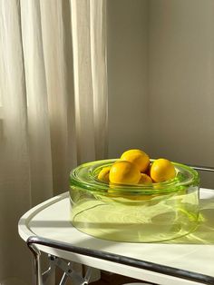 a glass bowl filled with lemons sitting on top of a table next to a window