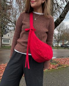 a woman standing in front of a tree wearing a red purse with a bow on it