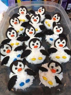 a plastic container filled with lots of cupcakes covered in frosting and penguins