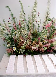 a table topped with lots of white and pink flowers next to each other in front of a wall