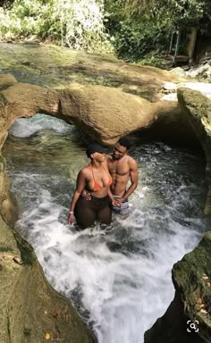 two people standing in the water near rocks