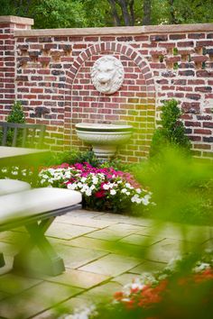 a brick wall with a fountain surrounded by flowers