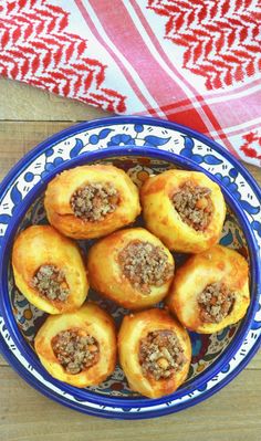 a blue bowl filled with sausage rolls on top of a wooden table next to a red and white towel