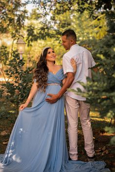 a pregnant woman in a blue dress standing next to a man with his arm around her belly